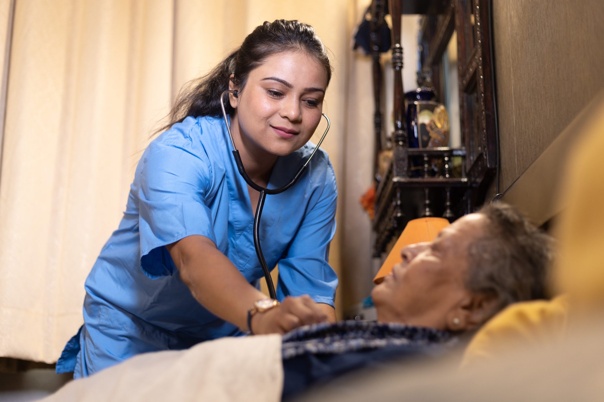 Healthcare worker in blue scrubs examining patient with stethoscope