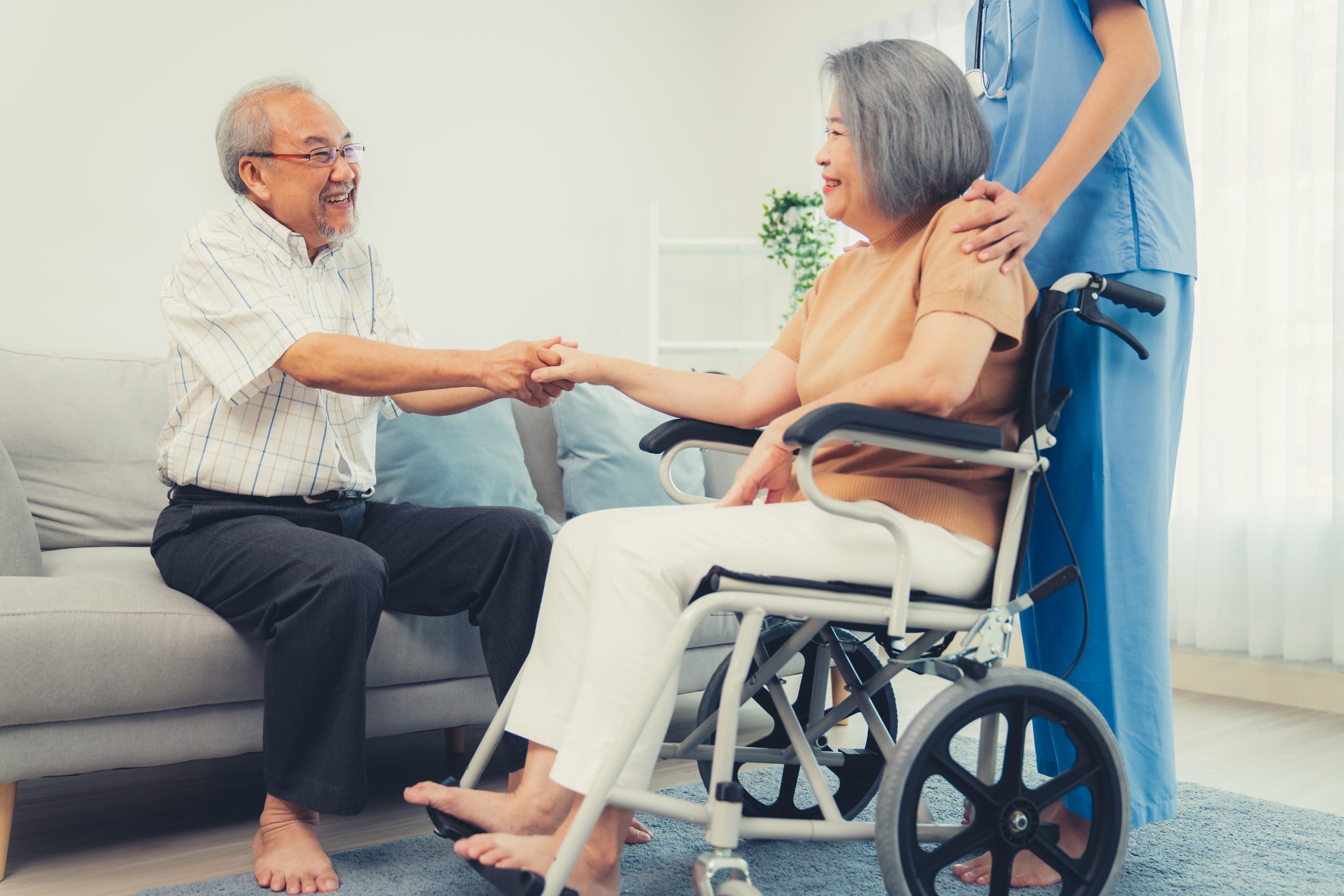 Senior man holding hands with elderly woman in wheelchair while caregiver assists